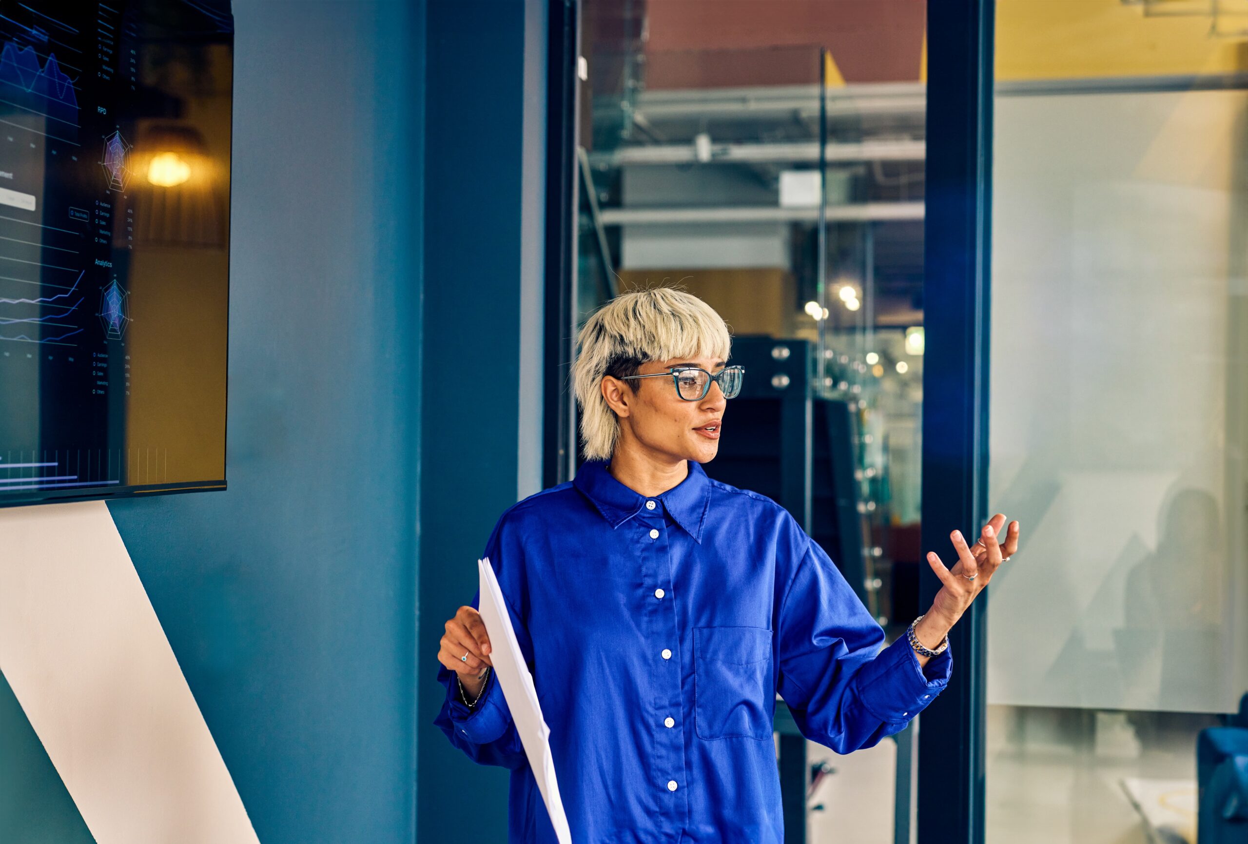 Mujer joven en su trabajo exponiendo una presentación al resto del equipo.