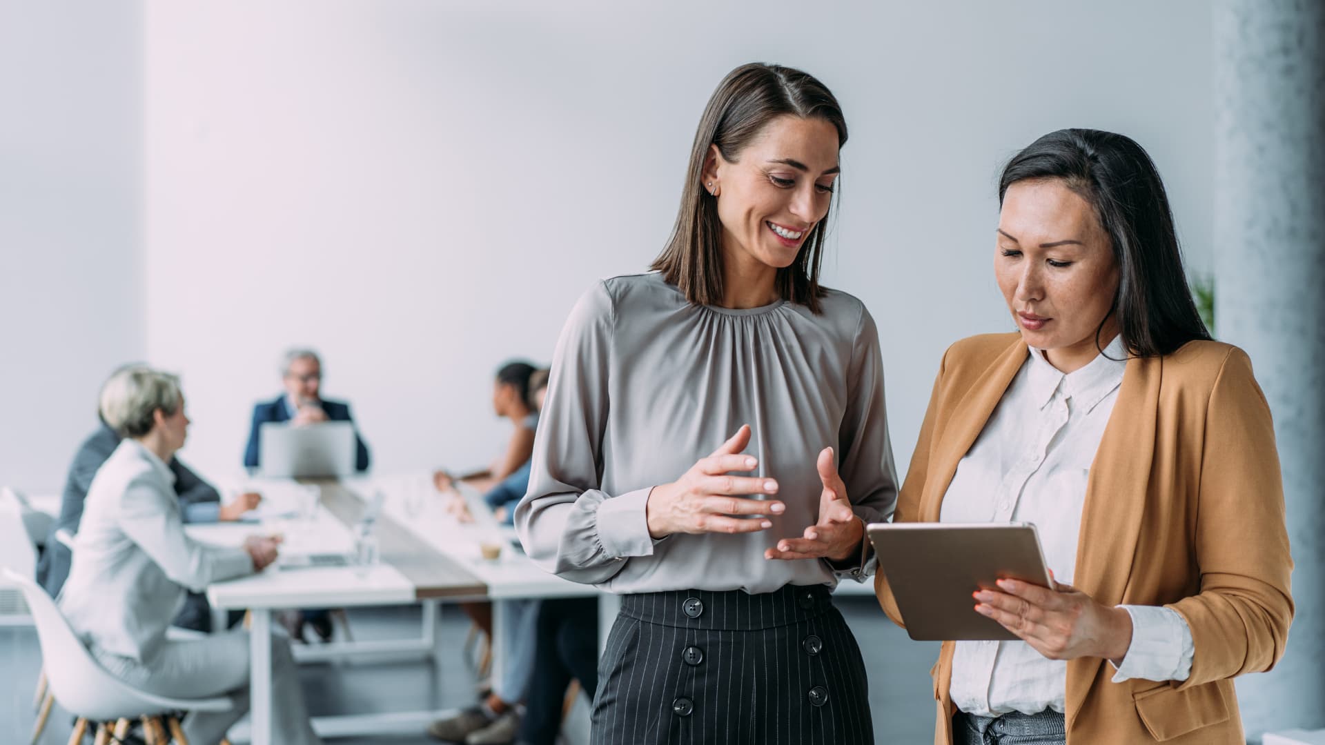 Mujeres charlando en el trabajo con una reunión de fondo.