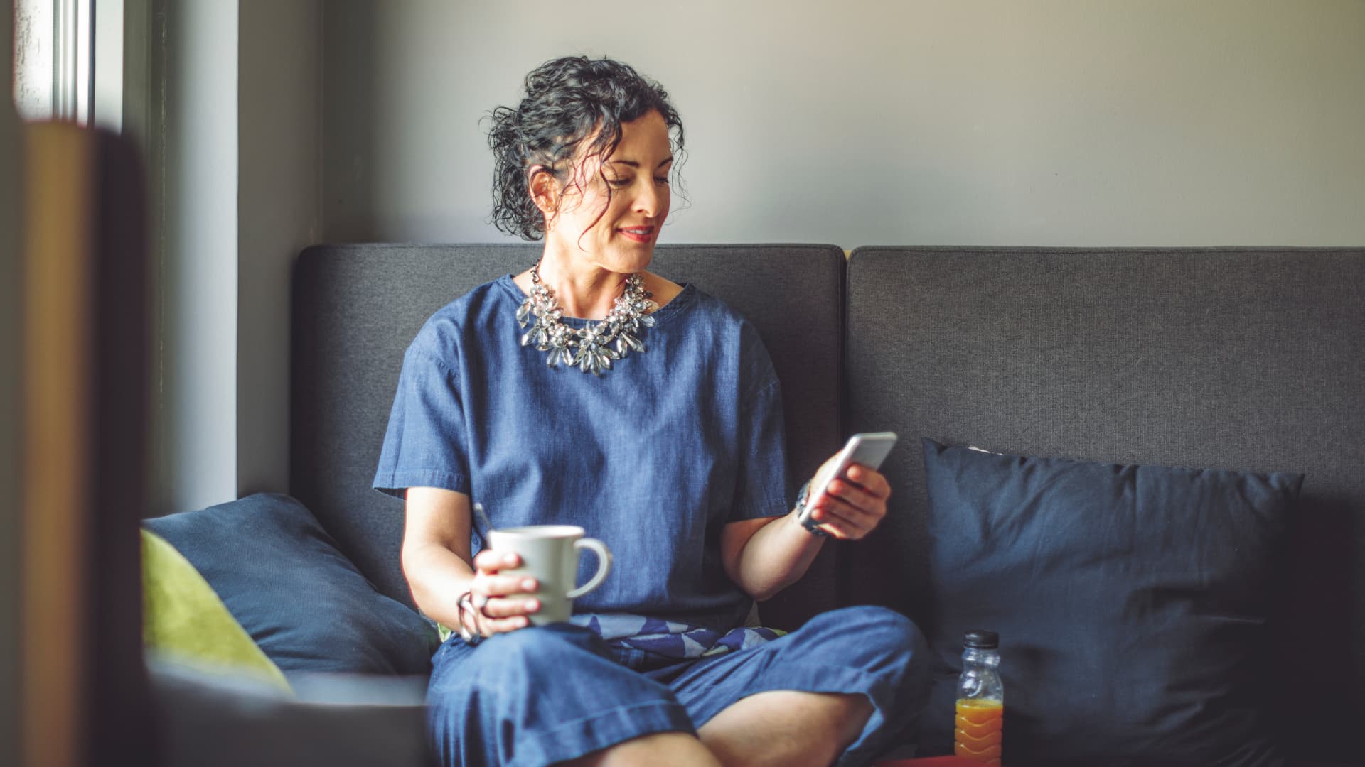 Mujer sentada en el sofá tomando un café y mirando el móvil.