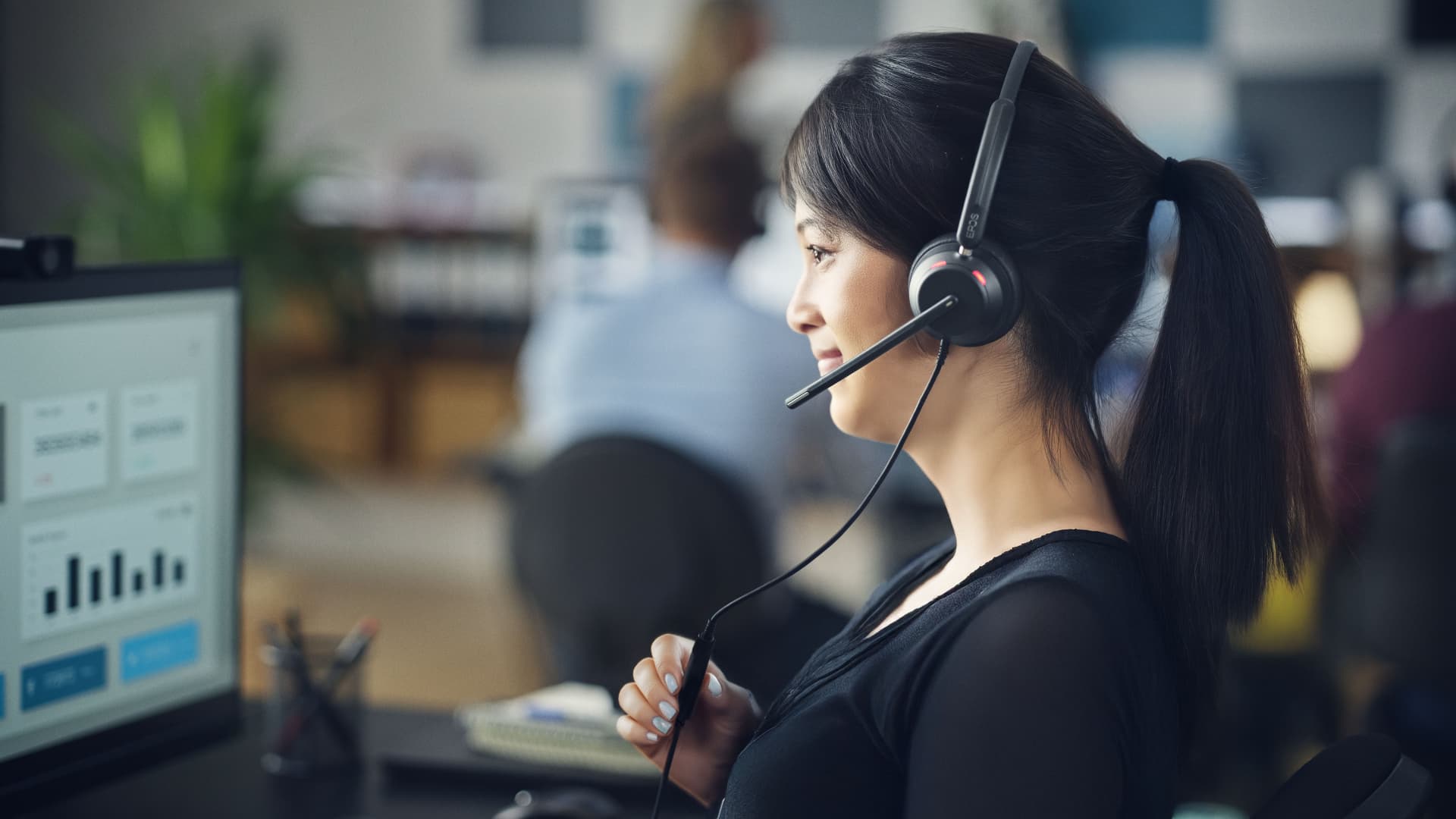 Mujer agente en su puesto de trabajo Contact Center con auriculares para cancelación de ruido para mejorar la productividad y la atención al cliente.