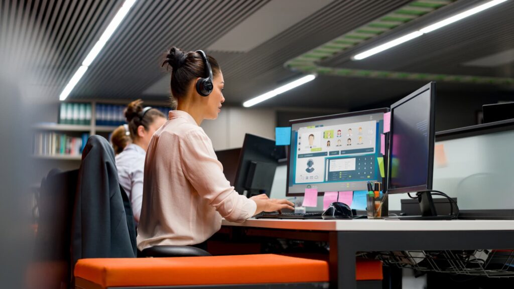 Mujer en su puesto de trabajo de atención al cliente mejorando la experiencia del usuario gracias a la omnicanalidad: teléfono, mensajes, chat.