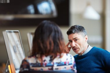 Hombre y mujer en su puesto de trabajo de tecnología e informática hablando.