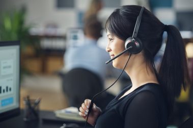 Mujer agente en su puesto de trabajo Contact Center con auriculares para cancelación de ruido para mejorar la productividad y la atención al cliente.